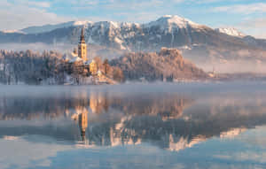 白雪覆蓋的山脈和教堂島在霧氣瀰漫的湖泊中於黎明時分倒映。