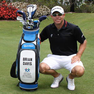 高爾夫球手 Brian Davis 在綠色球場上蹲在其高爾夫球袋旁。