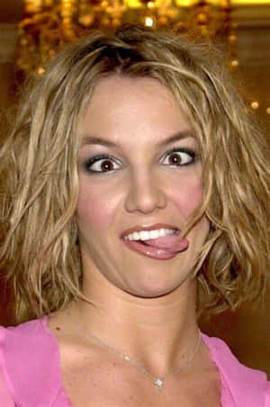 Britney Spears 身穿粉紅色上衣，頑皮地伸出舌頭。
