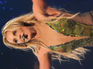 Shakira 在舞台上唱歌，身穿閃亮綠色服裝，金色長髮。