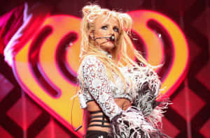 Britney Spears 在舞台上表演，身穿白色蕾絲服裝，帶有羽毛袖。