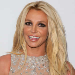 Britney Spears 穿著閃亮上衣，長長的金色頭髮，微笑著。
