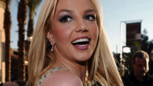 Britney Spears 在戶外活動中，與棕櫚樹和建築物一起微笑。