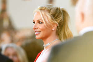 Britney Spears 在正式活動中穿著紅色連衣裙和鑽石頸鏈微笑。