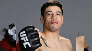 UFC拳手舉起黑色手套，胸口可見紋身，灰色抽象背景。