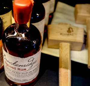 一瓶 Breckenridge Spiced Rum，木質包裝，置於深色表面上。 — 木紋 壁紙
