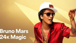 Bruno Mars 戴著太陽眼鏡和金鏈，穿著紅色襯衫，在金色背景前。
