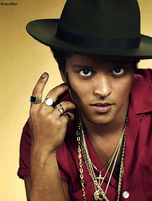 Bruno Mars 戴著黑色軟呢帽和紅色襯衫，佩戴金色珠寶，為照片擺姿勢。