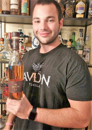 男人在酒架前拿著Avion Tequila酒瓶。