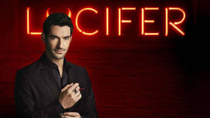 身穿黑色西裝的男子在磚牆上的紅色霓虹燈 Lucifer 標誌下拿著筆。