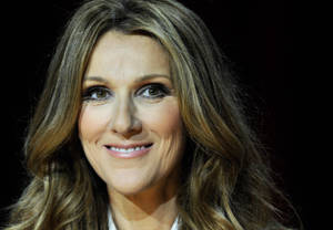 Celine Dion 在深色背景下留著長捲髮微笑。