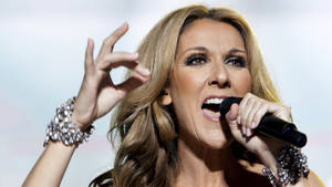 Celine Dion 在舞台上唱歌，戴著閃閃發光的手鐲，做出富有表現力的手勢。