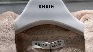 白色衣架上嘅米色絨毛衣物，附有SHEIN品牌標籤同尺寸標籤。