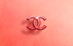 一個紅色 Chanel 標誌氣球漂浮在帶有紋理的珊瑚色背景上。