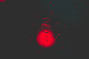 發光的紅色球體透過黑暗表面上的雨滴觀看。