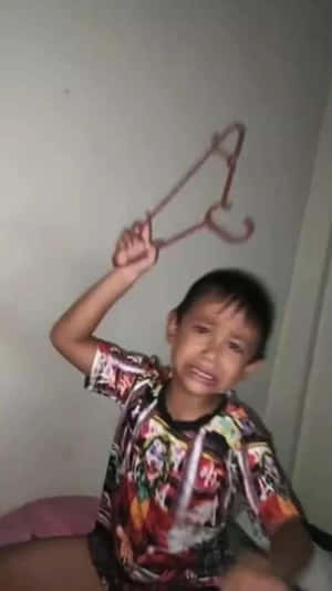 一個孩子拿著衣架，在室內頑皮地微笑。