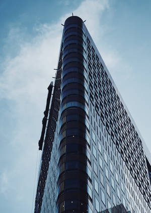 高聳的現代建築，帶有彎曲玻璃和幾何窗戶，襯著藍天。 — 建築 壁紙