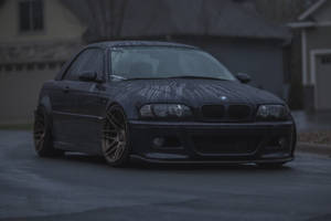 黑色BMW M3雙門轎跑車，金色輪圈，停在潮濕街道上，暮色中。