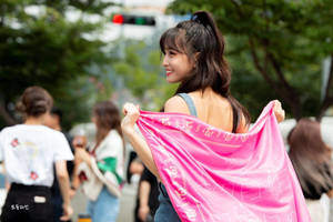 年輕女子微笑著在城市街道上舉起一條粉色圍巾。