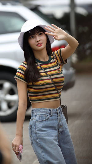 年輕女性穿著條紋上衣和牛仔褲，戴著白色帽子揮手。