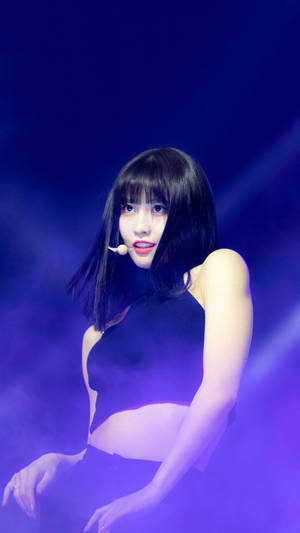 一位穿著黑色服裝的女性表演者在帶有煙霧的紫色舞台燈光下。