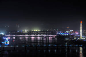 城市夜景，有燈光璀璨的橋樑和一個頂端有火焰的高大紀念碑。 — 韓國 壁紙