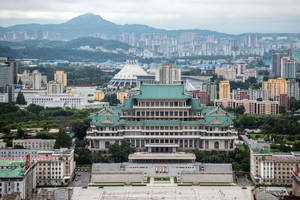 在密集的城市區域中，一座擁有綠色屋頂的大型傳統建築，背景是山脈。