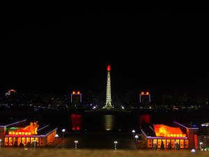 主體塔在夜晚亮起，建築物發光，水面倒影。