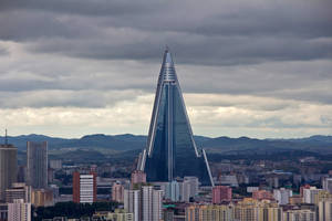 一座高大的玻璃金字塔建築在多雲的天空下矗立於城市之上。 — 韓國 壁紙