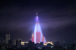 夜晚一座明亮照明的金字塔形建築，背景是城市天際線。 — 韓國 壁紙