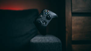 黑色Xbox手掣在昏暗房間的灰色扶手上，配有木質鑲板。 — 遊戲 壁紙
