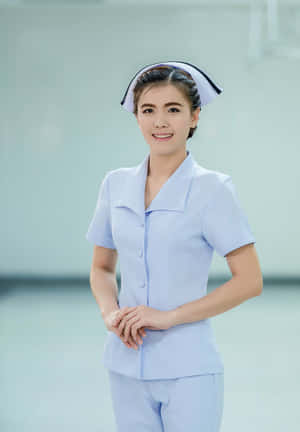 一位微笑的女護士穿著淺藍色制服和白色帽子，站在攝影棚內。