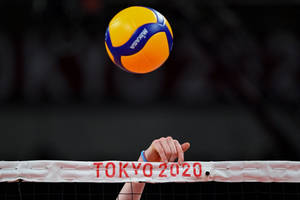 一隻手抓住標有 Tokyo 2020 的排球網，一個球懸浮在網上。