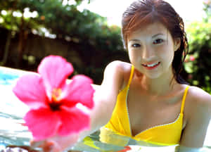 穿黃色泳衣的女性在泳池中手持粉紅色木槿花