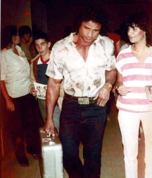 一個肌肉發達的男人帶著手提箱，穿著1980年代的服裝，穿過擁擠的室內派對。