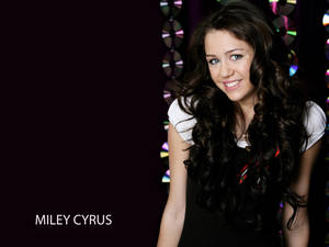 Miley Cyrus 在工作室中微笑，身後有CD燈光。
