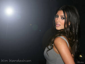 Kim Kardashian 穿著灰色上衣在聚光燈下，帶有鏡頭光暈。
