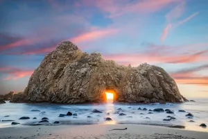 夕陽的光線穿過天然岩石拱門,照射在寧靜的海灘上。