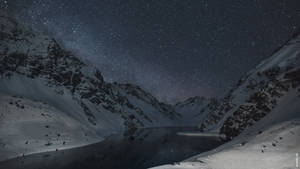 雪山環繞著寧靜湖泊中倒映的繁星夜空。