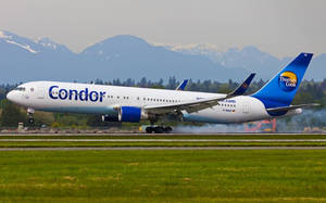 Condor Thomas Cook飛機在跑道上，背景有山脈和綠色田野。