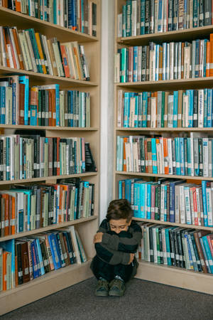 一個小男孩蜷縮在圖書館角落，周圍是書架。
