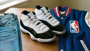 白色和黑色的Air Jordan 11運動鞋，搭配藍色牛仔褲和NBA外套，置於木頭上。