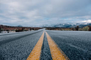 蜿蜒的道路在陰沉天空下通往積雪覆蓋的山脈。