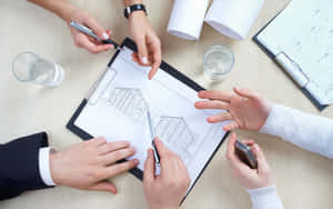 Four people reviewing architectural blueprints at a desk during a business meeting.