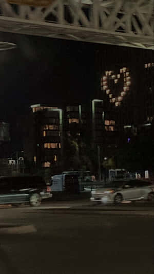 夜晚城市場景，有移動的汽車和建築物上的心形燈光顯示。