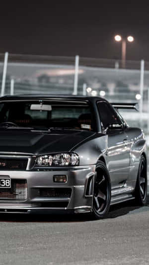 銀色日產Skyline GT-R在夜間停泊在賽車場上，在明亮的燈光下。