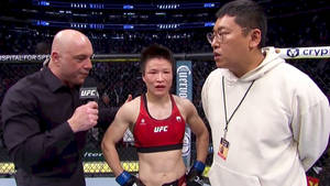UFC拳手在八角籠內接受訪問，旁邊有一位身穿白色連帽衫的男子。