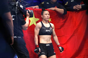 女性UFC拳手穿著黑色裝備站在帶有黃星的中國國旗前。