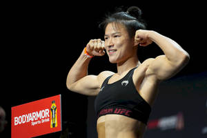 女性MMA拳手在稱重活動中穿著黑色UFC運動胸罩展示手臂。