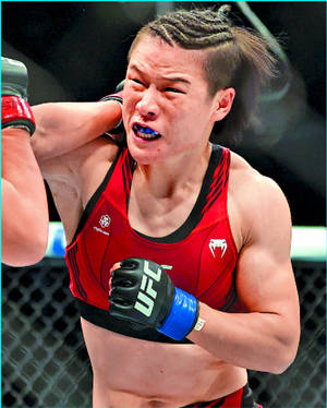 身穿紅色裝備的女性MMA拳手在八角籠內痛苦地扭曲表情。